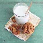 Almond milk in glass with almonds in bowl, on color wooden backg