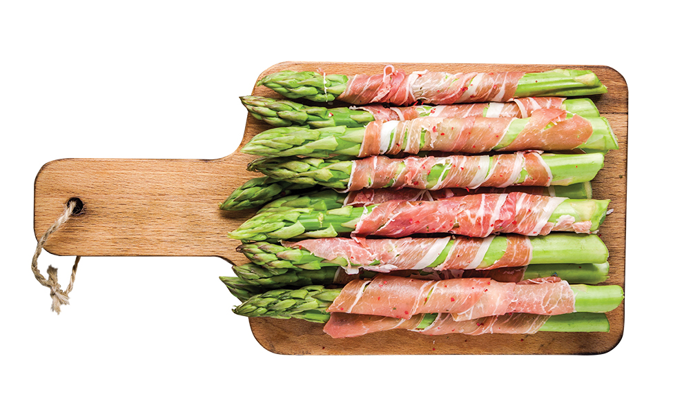 Fresh asparagus wrapped in Parma ham on a cutting board